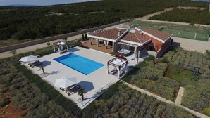 Una villa con piscina, mobiliario exterior y cancha de tenis.