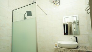 Un baño con cabina de ducha de vidrio, un lavamanos con encimera de mármol y un espejo sobre el lavamanos.