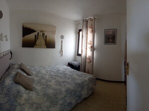 Une chambre à coucher avec un lit, un tableau, une fenêtre avec des rideaux et une porte.