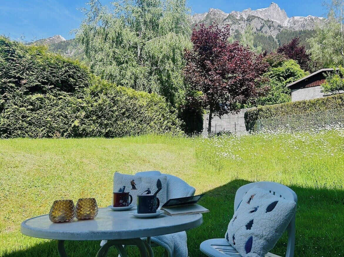 A round table with two glasses, a cup, and a book, set in a grassy area with a chair.