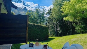Mesa redonda con un libro, dos tazas y una vela en un jardín con vista a la montaña.