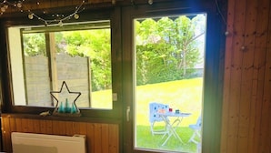 Una habitación con un panel de madera, un radiador y una ventana que da a un área verde con una silla afuera.