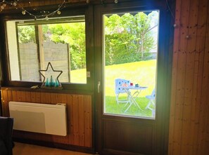 Ein Zimmer mit einer holzverkleideten Wand, einem Heizkörper und einem Fenster mit Blick auf eine grüne Fläche und einen Stuhl davor.