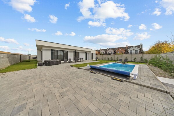 A modern house with a swimming pool, paved patio, and a small lawn area.