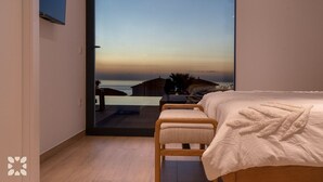 A bedroom with a large window, a bed, a bench, and a view of the sea. - Villa CARRERA by Abahana Villas (Benitachell)
