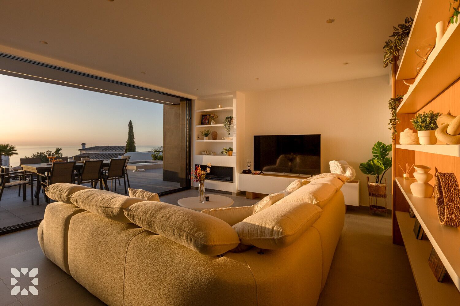 A modern living room with a large sofa, a TV, and a dining area with a view of the sea.