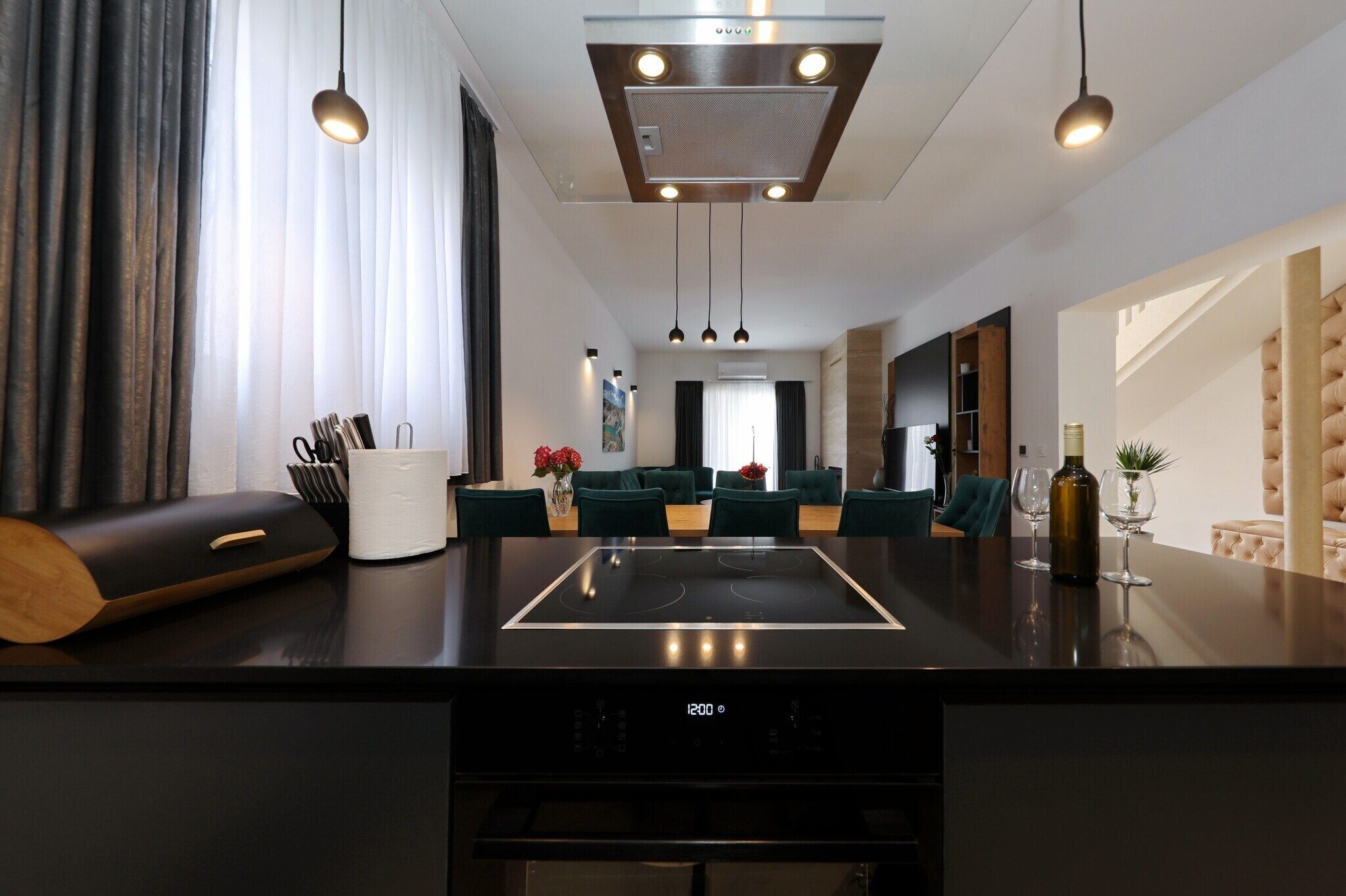 Une cuisine moderne dotée d’une cuisinière intégrée, un coin repas avec une table et des chaises noires, et un salon avec un canapé et une table basse.