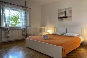 A bedroom with a bed, a radiator, a window with curtains, and a painting on the wall. - Apartment in a lush sea-view park (Poljica)