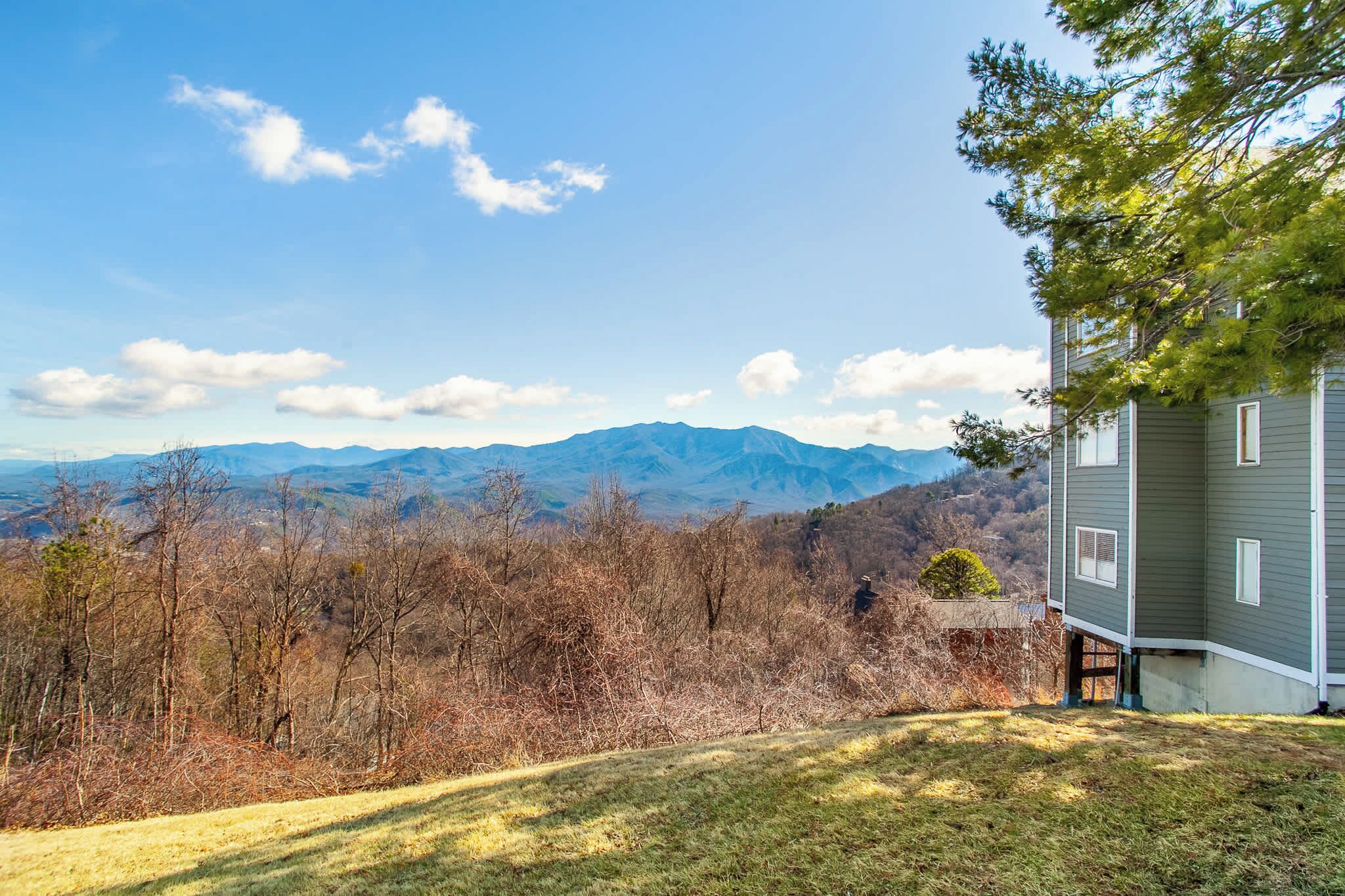 Une maison avec vue sur la montagne, une pelouse bien entretenue et un grand arbre au premier plan.