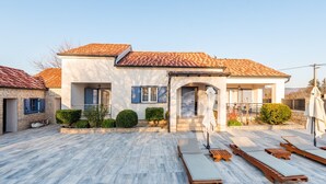 A modern house with a tiled roof, a covered patio with lounge chairs, and a well-maintained garden. - Villa near Zrmanja's canyon (Pridraga)