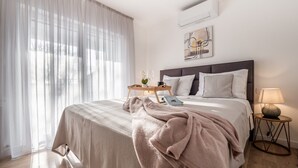 A neatly made bed with a beige blanket, a bedside table with a lamp, and a window with sheer curtains. - Villa near Zrmanja's canyon (Pridraga)