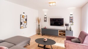 A modern living room with a grey sofa, a round coffee table, and a pink armchair. A flat-screen TV is mounted on the wall above a grey cabinet. - Villa near Zrmanja's canyon (Pridraga)