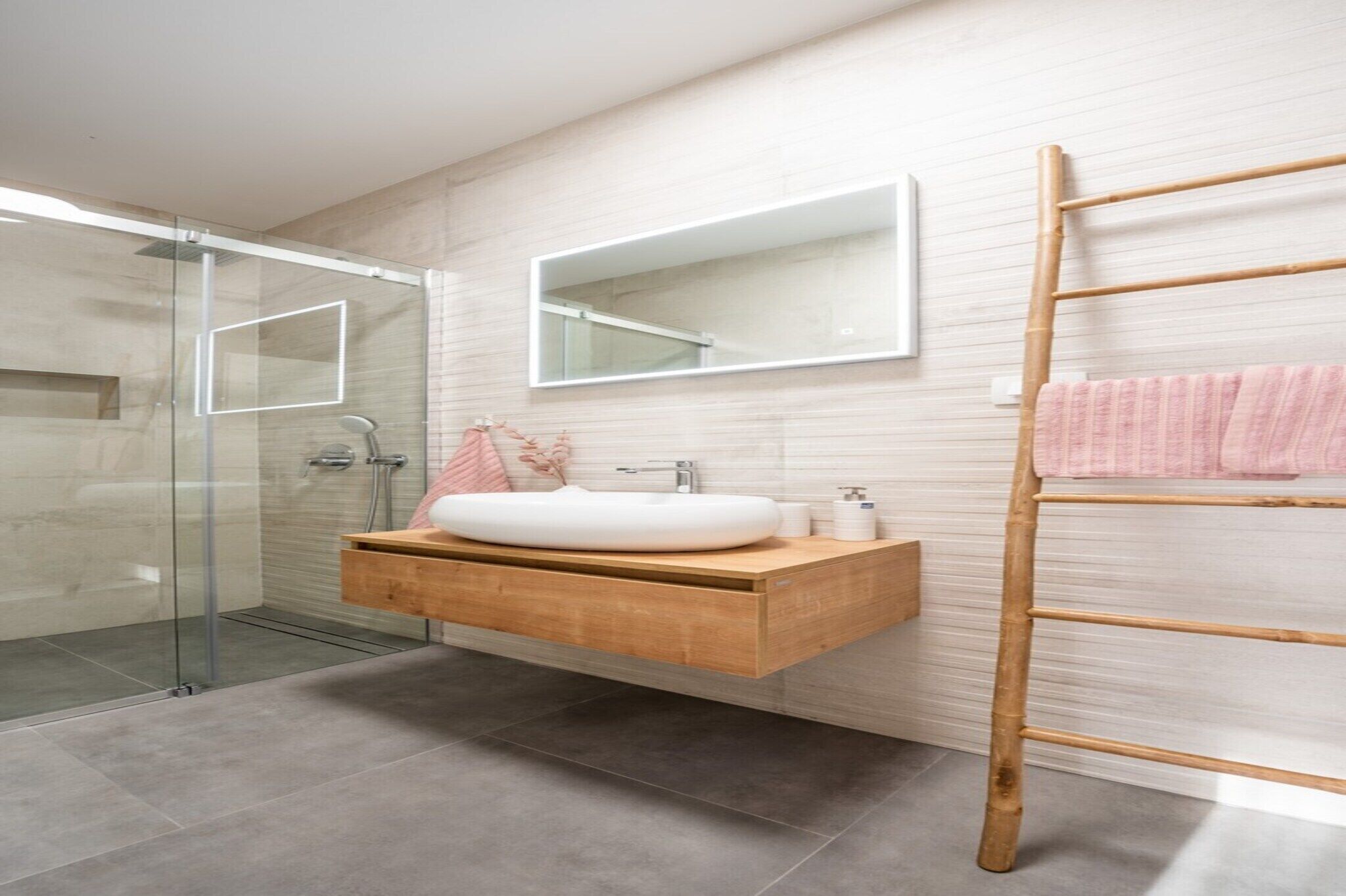 Une salle de bain moderne avec une douche à parois de verre, un meuble-lavabo en bois avec un vasque blanche, un miroir et un porte-serviettes en bambou.