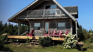 Een houten blokhut in rustieke stijl met een veranda, twee ramen en een rode deur.