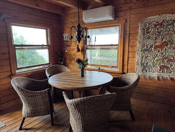 L’intérieur d’un chalet en bois, avec une table ronde, des chaises en osier, un lustre et une tapisserie ornée de motifs animaliers.