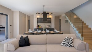 A modern living room with a sofa, a dining table set for four, and a staircase. - Villa Kalea with pool (Marceljani)