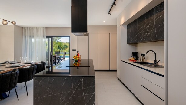 A modern kitchen with a central island, a dining area with a view, and a large window. - Villa Kalea with pool (Marceljani)