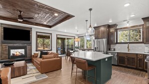 A modern kitchen with a large island, wooden cabinets, and a built-in fireplace. - East Zion New Build, Sleeps 12, Hot Tub, Rooftop Fire Pit & Game Room (Orderville)