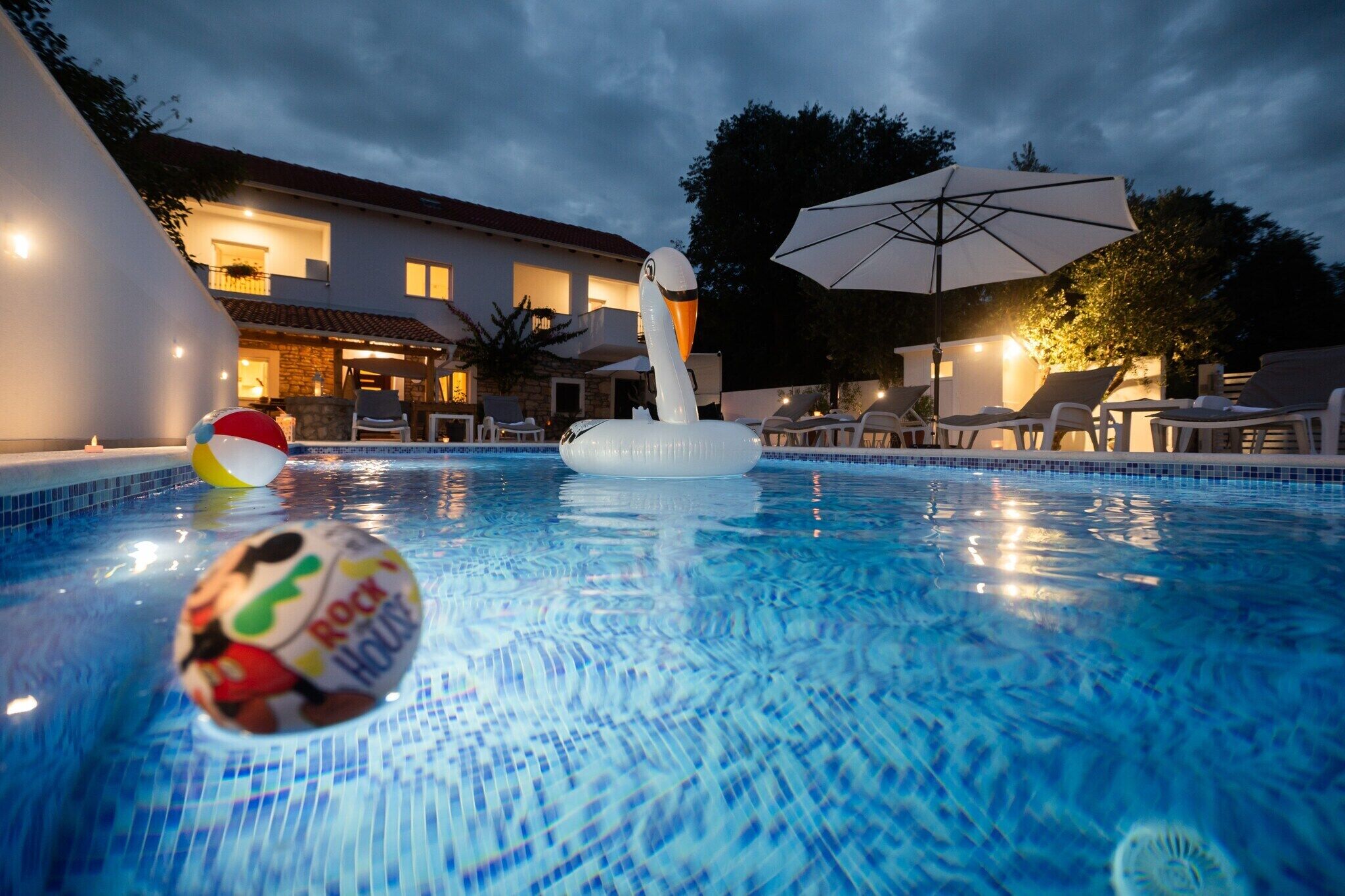 Una piscina con juguetes inflables, sillas de descanso y sombrillas.