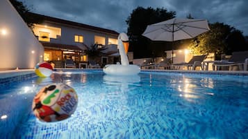 Una piscina con juguetes inflables, sillas de descanso y sombrillas.