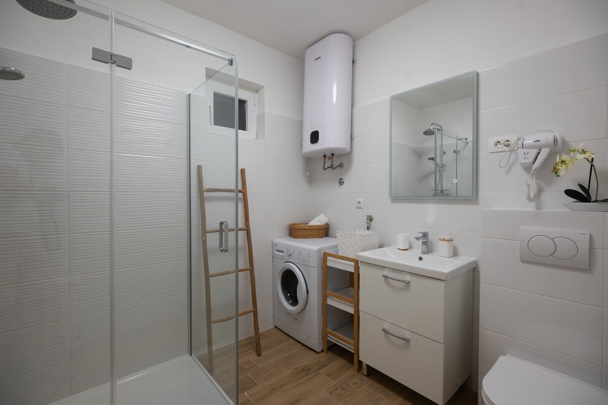 Un baño moderno con cabina de ducha de vidrio, lavadora integrada, lavamanos y un inodoro.