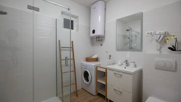 Un baño moderno con cabina de ducha de vidrio, lavadora integrada, lavamanos y un inodoro.