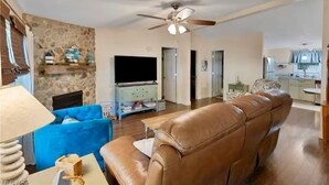 A living room with a brown leather sofa, a blue armchair, a stone wall, a flat-screen TV, and a ceiling fan. - GOTL Retreat, short walk to strip, 15 min to Spire (Geneva on the Lake)