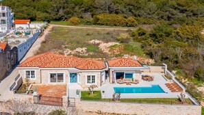 Ett stort hus med en swimmingpool, stenmurar och utsikt över en skogbeklädd kulle.