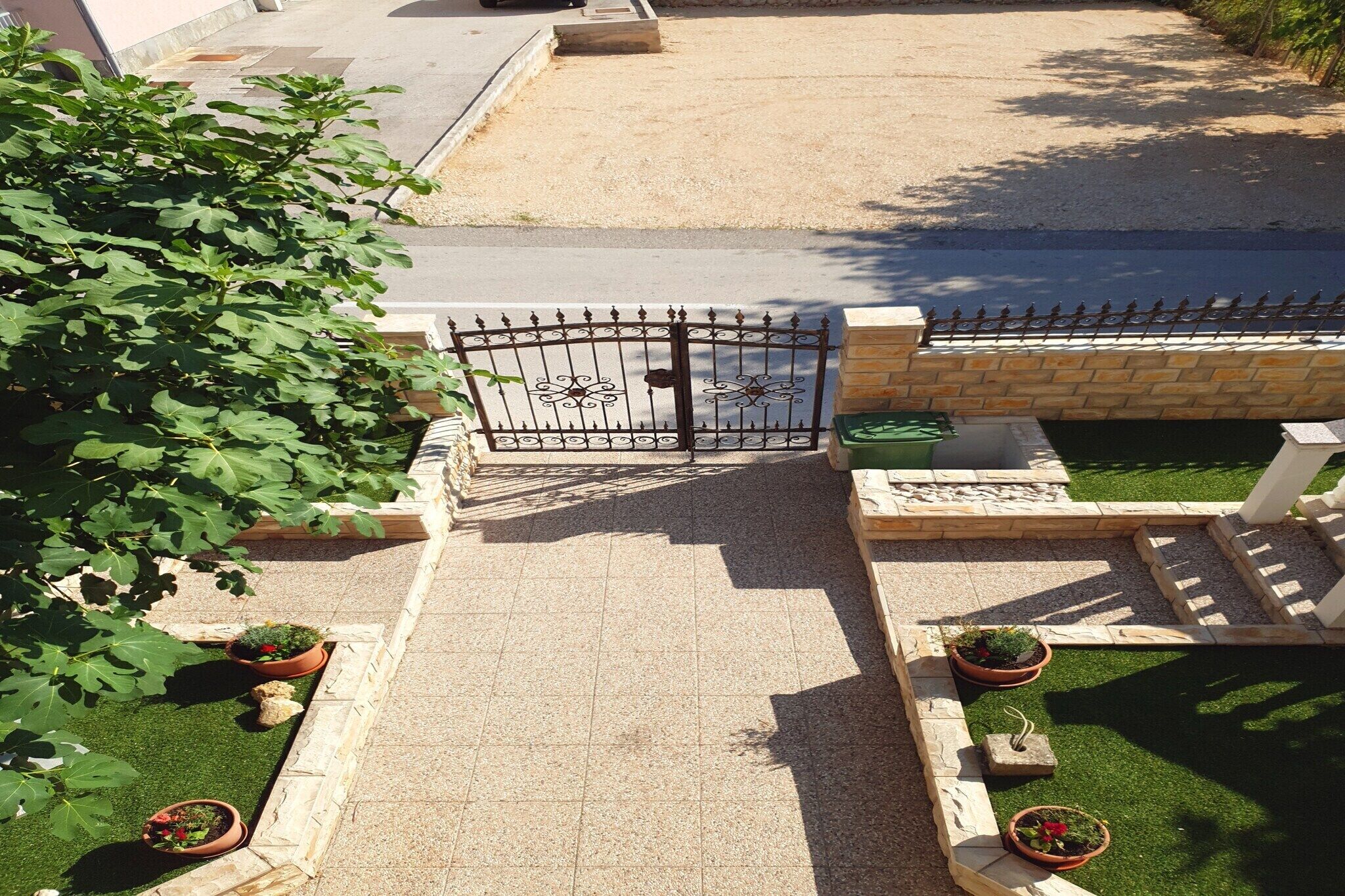 Une entrée fermée par un portail, avec un chemin pavé menant à un espace aménagé, agrémenté de plantes en pot et d’une petite pelouse.
