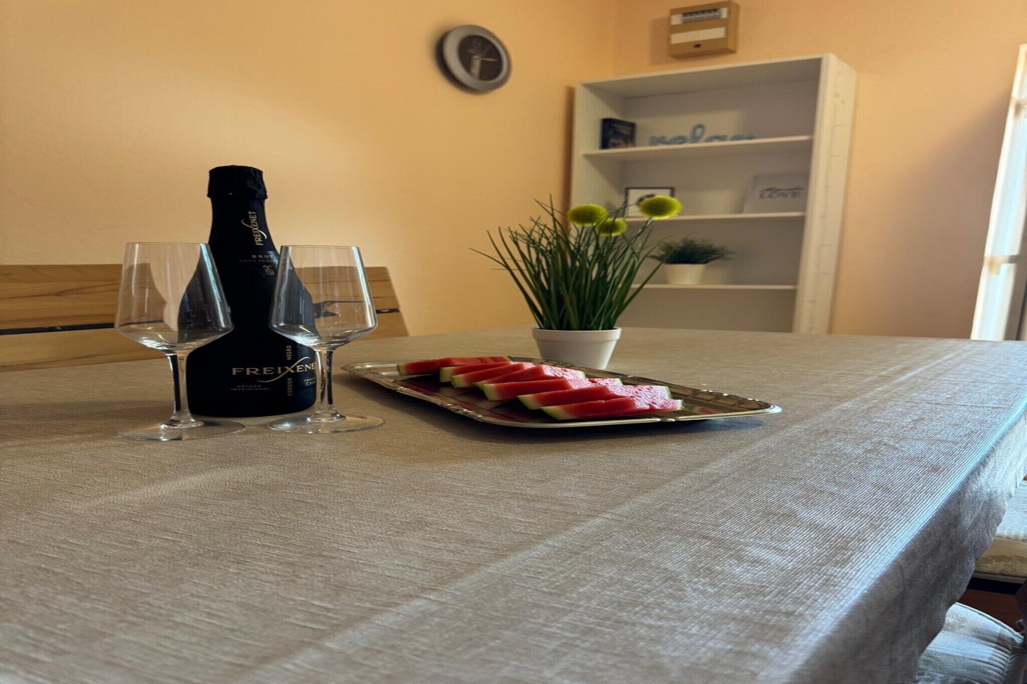 Une table avec une bouteille de champagne Freixenet, deux verres et une assiette de tranches de pastèque.