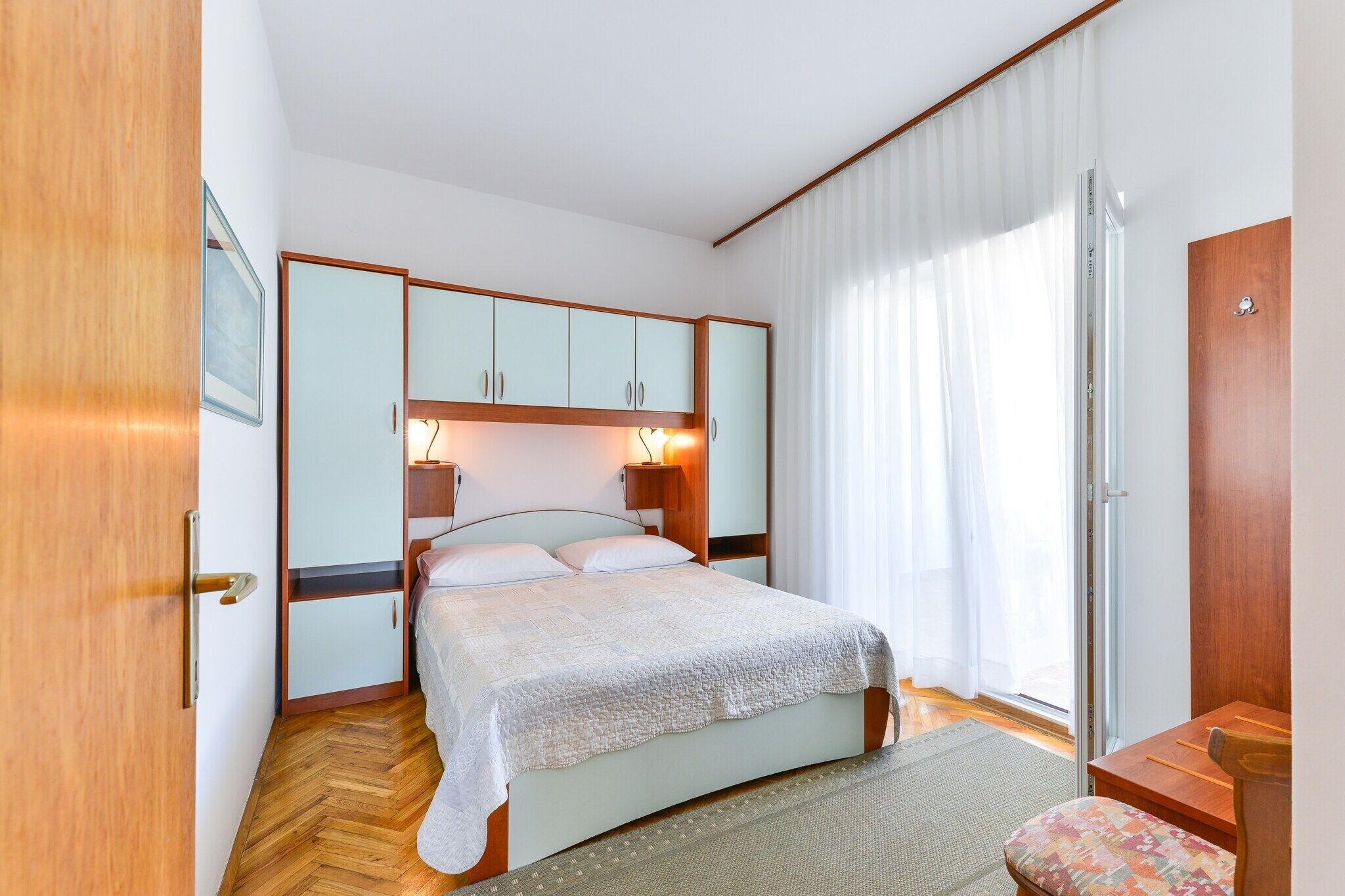 Une chambre à coucher avec un lit, une armoire en bois, des lampes de chevet et une fenêtre avec des rideaux.