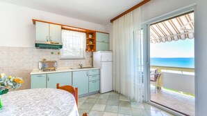 A kitchen with a view of the sea, a dining table with chairs, and a refrigerator.