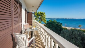 A balcony with a view of the sea, a table with chairs, and a window with shutters. - Seaside Tranquil Stay for 4 (Vir)