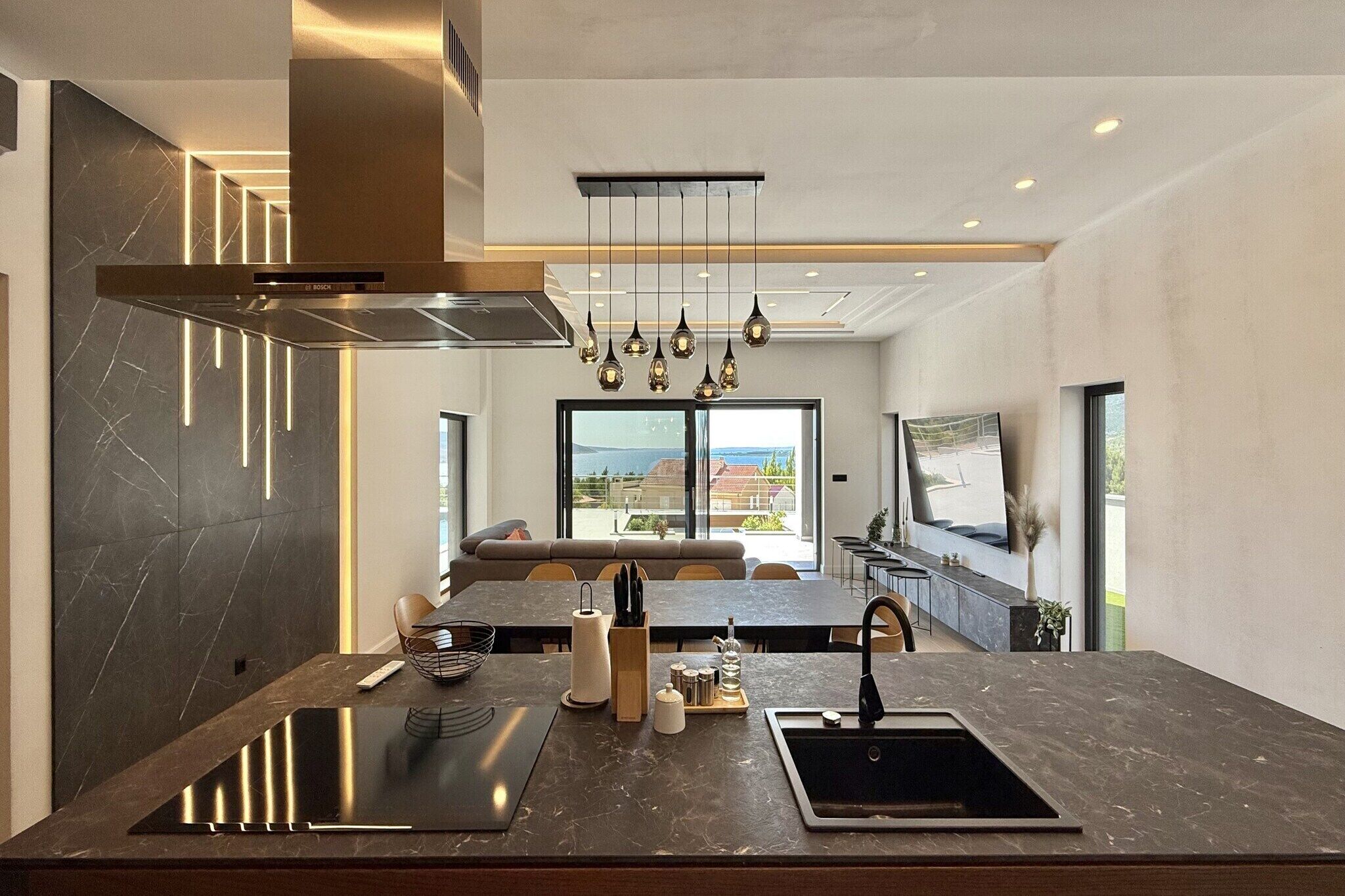 Une cuisine moderne dotée d’un îlot central, d’appareils électroménagers en acier inoxydable et de luminaires suspendus.