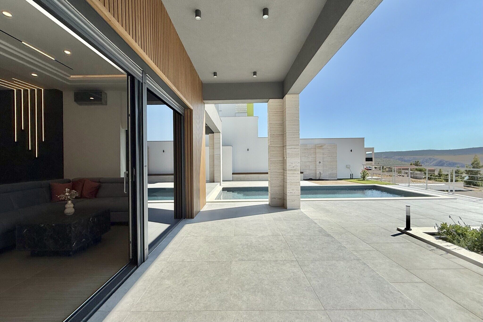 Un espace de vie extérieur moderne, doté d’une piscine, d’un coin salon avec un canapé et une table basse, et offrant une vue sur le paysage environnant.