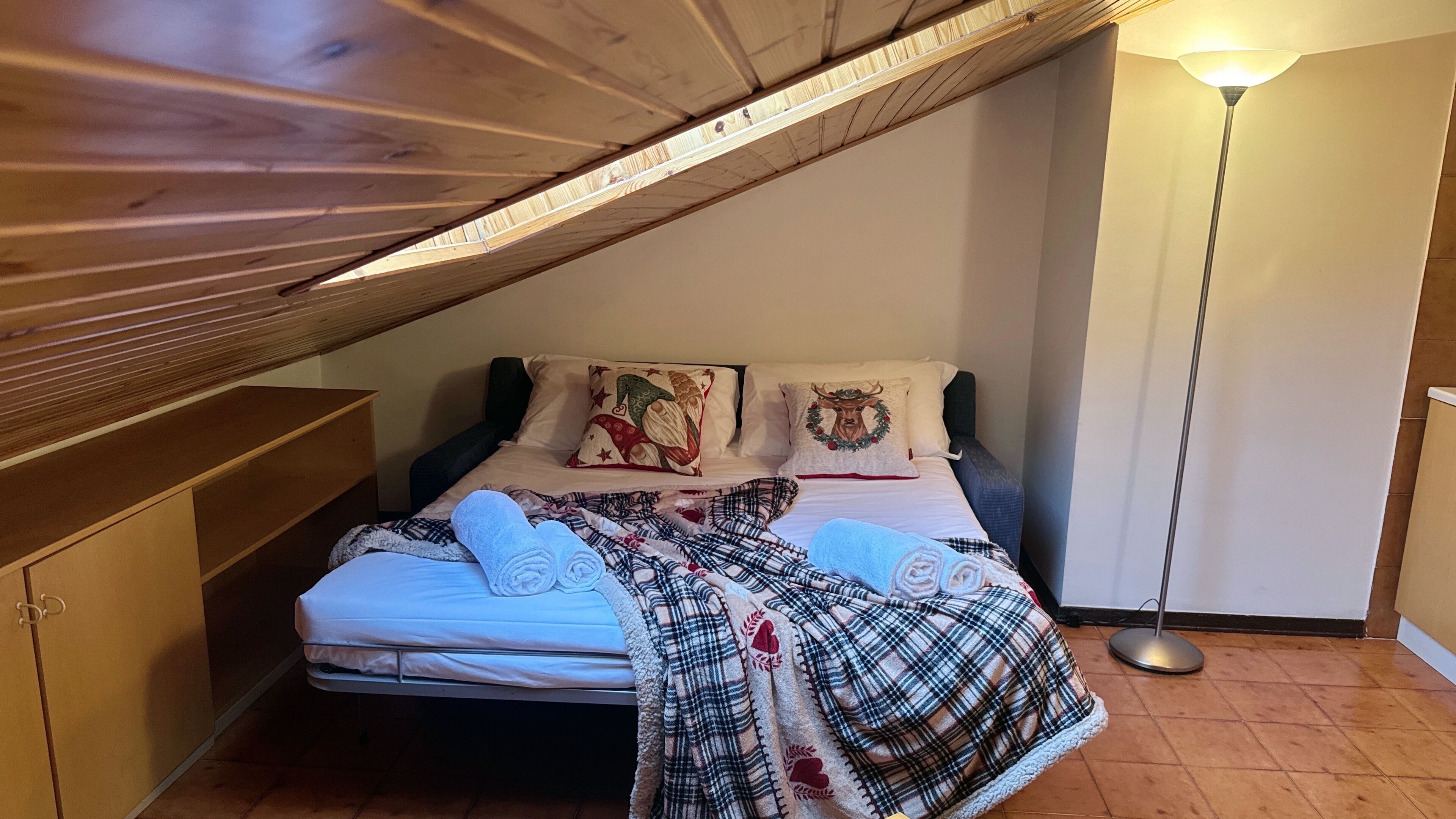 Um quarto de sótão acolhedor, com teto inclinado, cama com roupa de cama xadrez e um abajur.