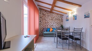 Un salón acogedor con pared de piedra, una mesa de comedor con sillas, un sofá con cojines de colores y un televisor sobre un mueble.