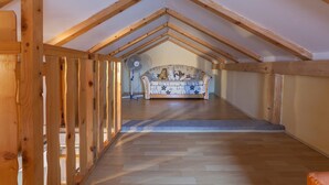 Una habitación con techo inclinado, vigas de madera, un sofá estampado y un ventilador.