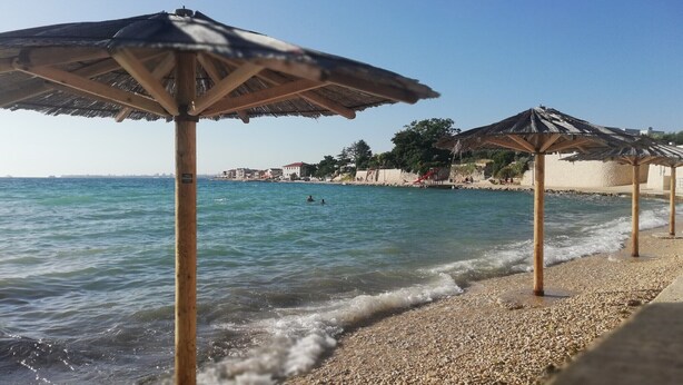 Una playa con costa pedregosa, sombrillas de madera y mar azul cristalino.
