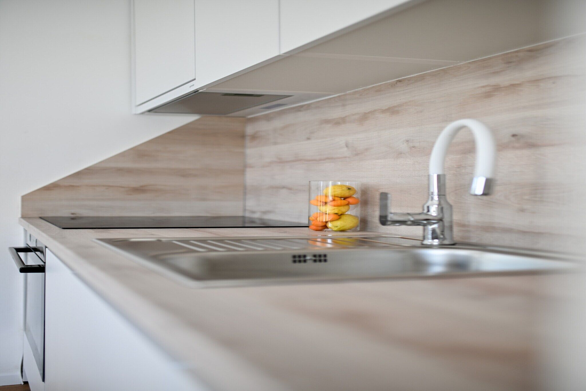 Una cocina con un lavamanos de acero inoxidable, armarios blancos y un protector de pared de madera.