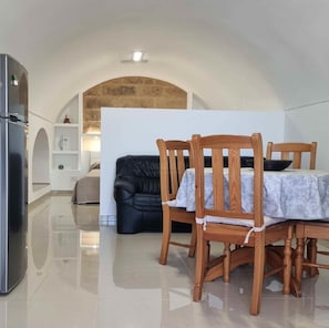 Ein Essbereich mit einem Tisch für vier Personen, einer schwarzen Couch und einem Kühlschrank.
