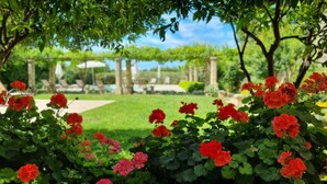 A garden with red geraniums and a clear view of a pool and lounge chairs in the background. - Altra Meta Palace by LoveSud (Gagliano del Capo)