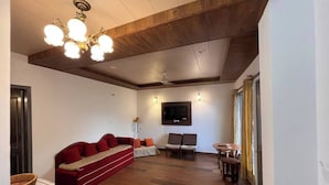 Una sala moderna con un sofá rojo, dos sillones, techo de madera, televisor de pantalla plana y una mesa de comedor.