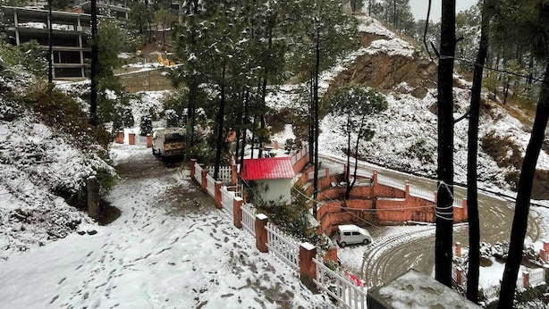 Un paisaje nevado con un edificio de techo rojo, una valla blanca y un muro de piedra.