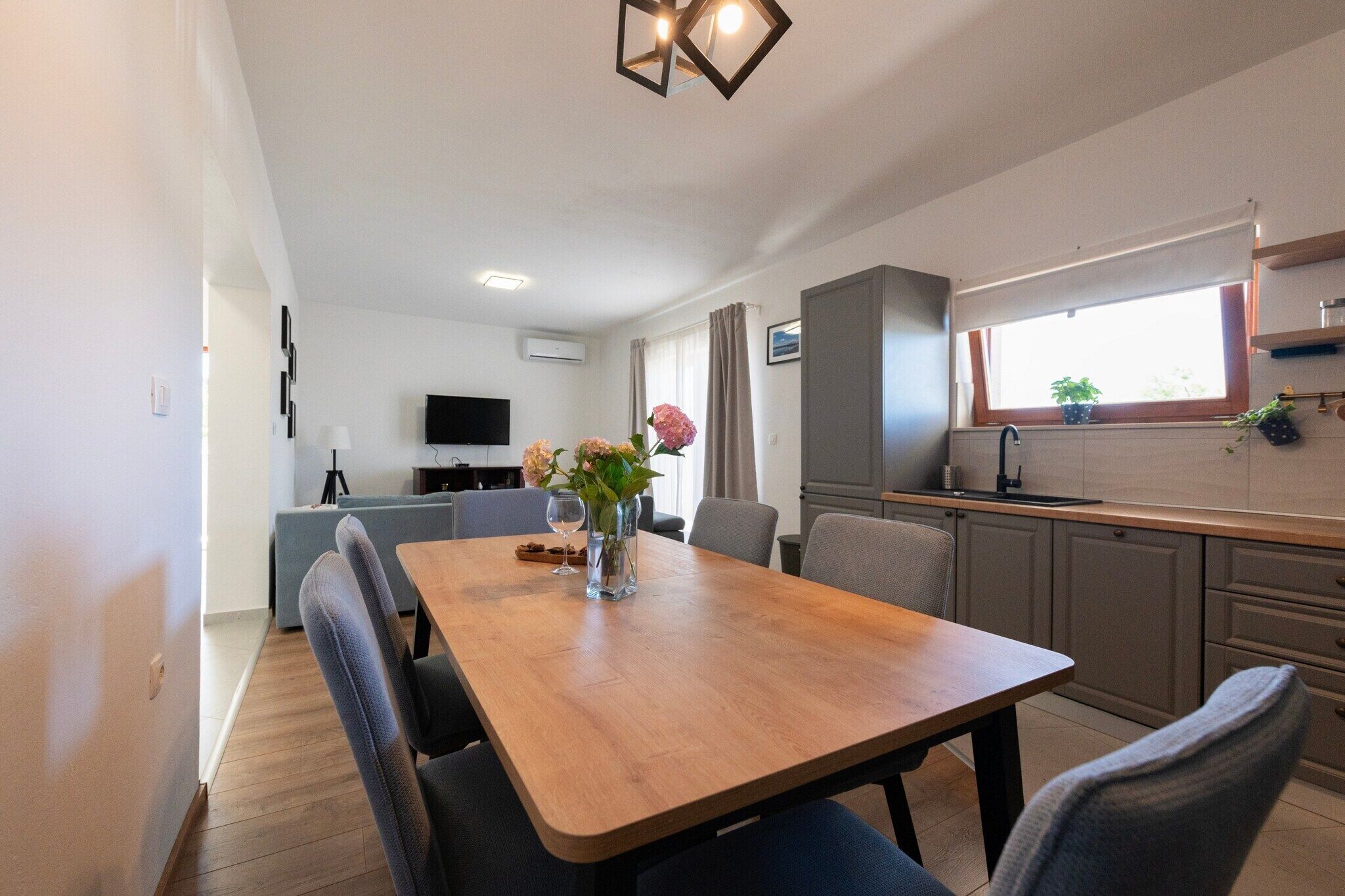 A modern kitchen with a wooden table, chairs, and a vase with flowers.