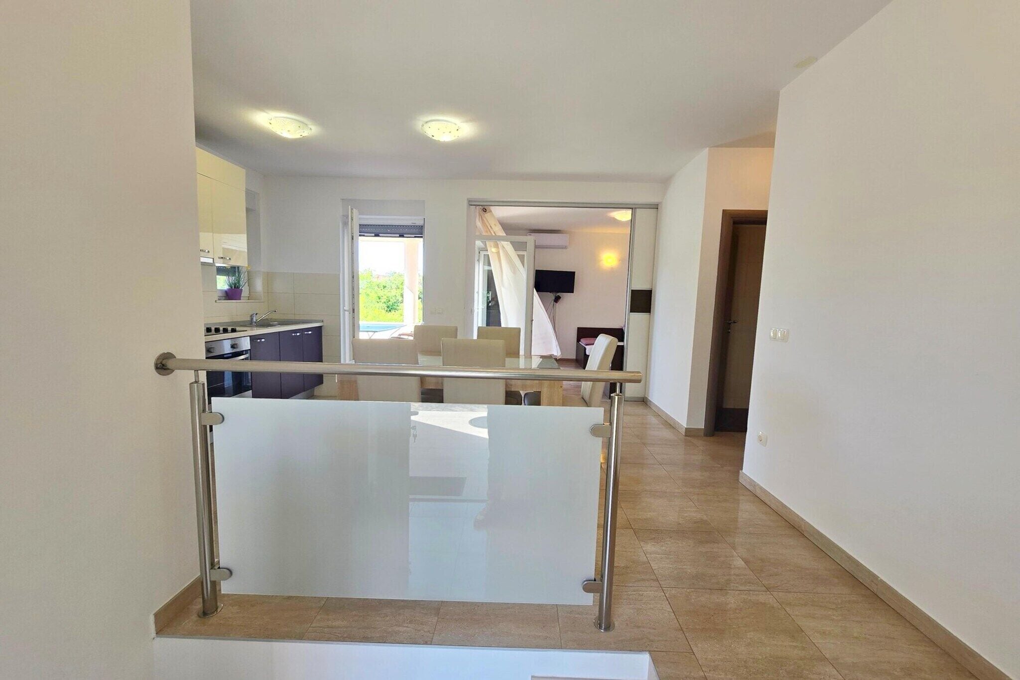 A modern interior with a glass railing, a kitchen area, and a staircase leading to another room.