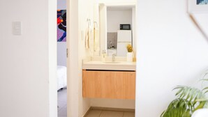 A bathroom with a white sink, wooden cabinets, a mirror, and a small plant. - Home office apartment with a fully equipped, comfortable desk, Roca (General Roca)