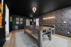 Une pièce avec une table de ping-pong, une petite table et un mur orné d’un motif floral.