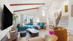 Ein modernes Wohnzimmer mit einem großen Flachbildfernseher, einem blauen Ecksofa, einem Couchtisch und einer Treppe mit Holzwand.