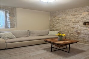 Un salon avec un mur en pierre, un canapé, une table basse en bois et un vase rempli de fleurs.